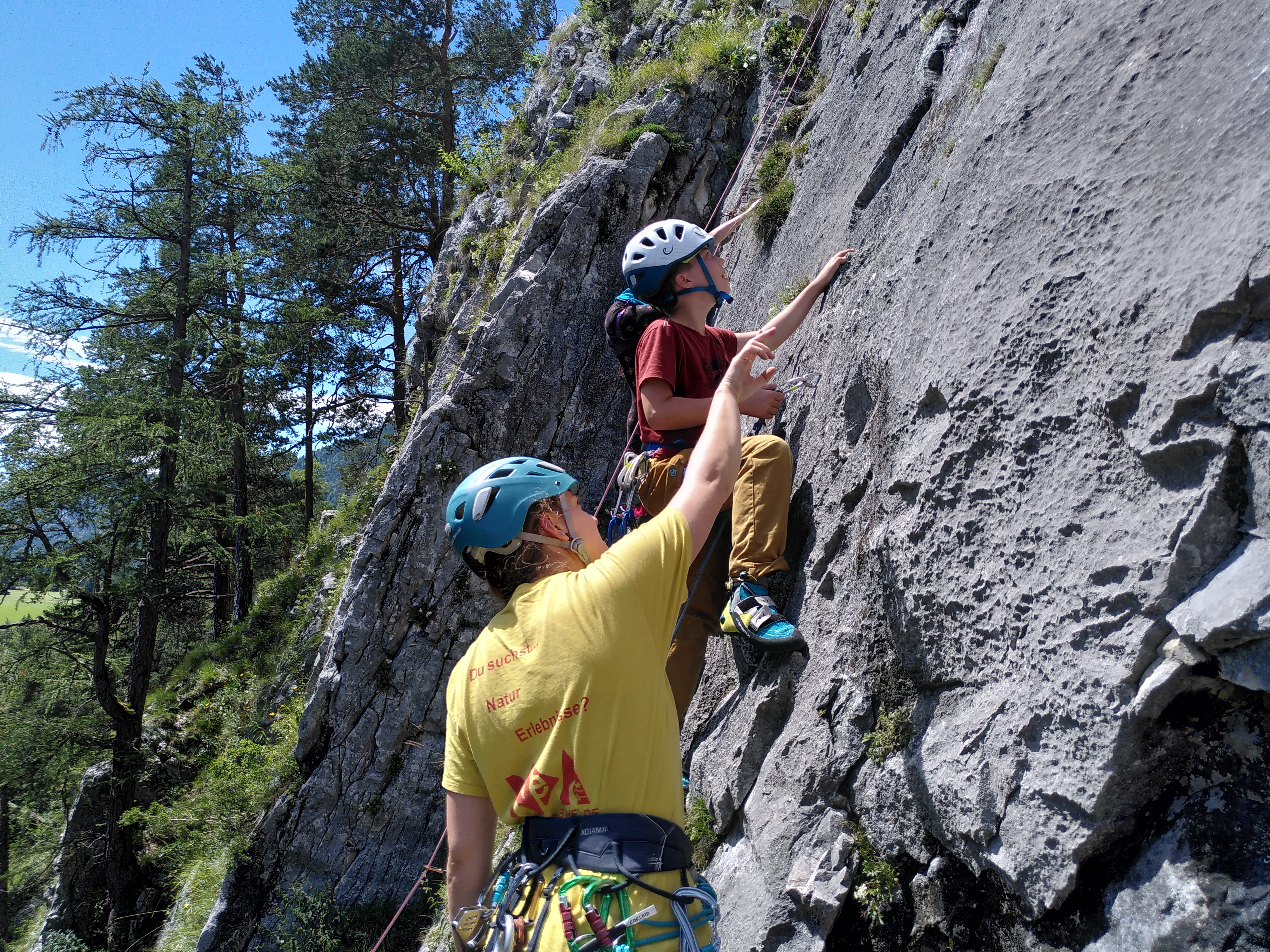 Eine Klettertrainerin hilft einem Kind beim Klettern am Fels.
